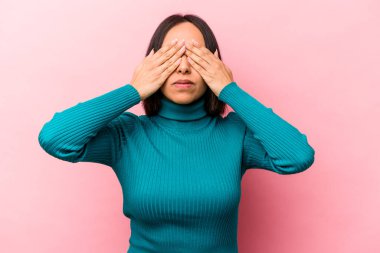 Pembe arka planda izole edilmiş genç İspanyol kadın elleriyle gözlerini kapatmaktan korkuyor..
