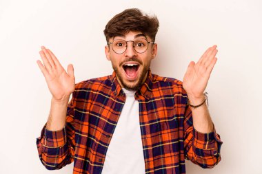 Latin kökenli genç bir adam beyaz arka planda izole edilmiş. Hoş bir sürprizle karşılaşıyor, heyecanlı ve el kaldırıyor..