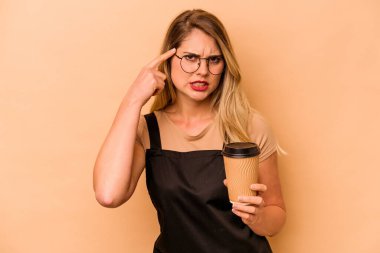 Restoran garsonu Kafkasyalı kadın elinde bej arka planda izole edilmiş kahve tutuyor işaret parmağıyla yaptığı hayal kırıklığı jestini gösteriyor..
