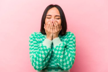 Pembe arka planda izole edilmiş genç İspanyol kadın bir şeye gülüyor, elleriyle ağzını kapatıyor..