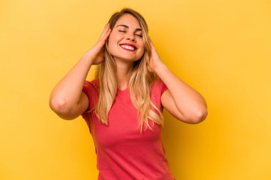 Sarı arka planda izole edilmiş genç beyaz kadın ellerini başının üstünde tutarak neşe içinde gülüyor. Mutluluk kavramı.