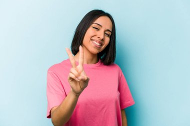 Mavi arka planda izole edilmiş genç İspanyol kadın iki numarayı parmaklarıyla gösteriyor..