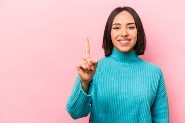 Pembe arka planda izole edilmiş genç İspanyol kadın bir numarayı parmağıyla gösteriyor..