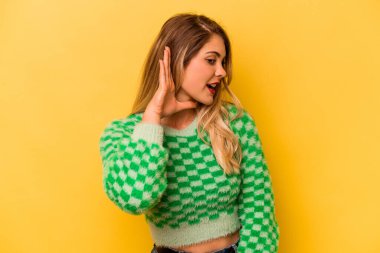 Sarı arka planda izole edilmiş genç beyaz kadın bir dedikoduyu dinlemeye çalışıyor..