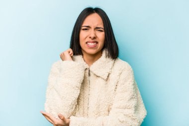 Genç İspanyol kadın mavi arka planda izole edilmiş, dirsek masajı yapıyor, kötü bir hareketin ardından acı çekiyor..