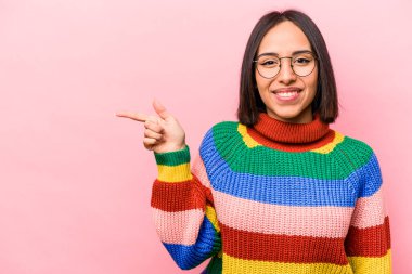 Pembe arka planda izole edilmiş genç İspanyol kadın işaret parmağıyla işaret ederek gülümsüyor..