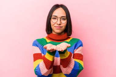 Genç İspanyol bir kadın pembe arka planda izole edilmiş. Elinde avuç içi olan bir şeyle kameraya sunuyor..
