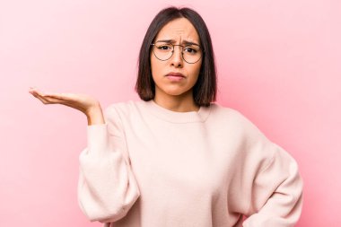Genç İspanyol kadın pembe arka planda izole edilmiş şüphe içinde ve sorgulama sırasında omuzlarını silkiyor..
