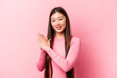 Pembe arka planda izole edilmiş genç Çinli kadın enerjik ve rahat hissediyor, ellerini ovuşturuyor..