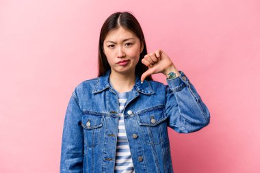 Pembe arka planda izole edilmiş genç Çinli bir kadın baş parmağını aşağı gösteriyor ve hoşlanmadığını ifade ediyor..