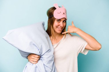Mavi arka planda izole edilmiş pijama giyen beyaz bir kadın cep telefonu hareketini parmaklarıyla gösteriyor..