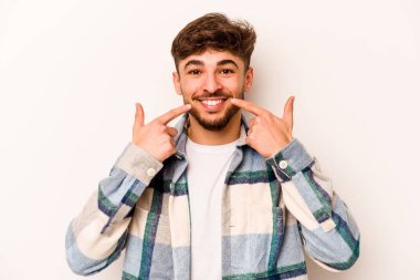 Beyaz arka planda izole edilmiş genç İspanyol adam gülümsüyor, parmaklarını ağıza doğrultuyor..