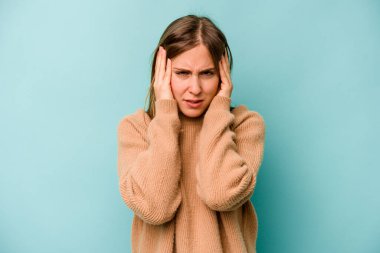 Kafkasyalı genç bir kadın mavi arka planda izole edilmiş, başı ağrıyor, yüzüne dokunuyor..