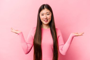 Pembe arka planda izole edilmiş genç Çinli kadın kollarıyla ölçek oluşturuyor, mutlu ve kendinden emin hissediyor..