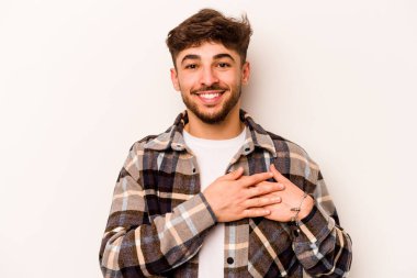 Beyaz arka planda izole edilmiş genç İspanyol bir adam, dost canlısı bir ifadeye sahip, avuçlarını göğsüne bastırıyor. Aşk konsepti.