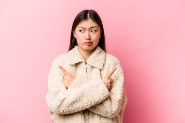 Pembe arka planda izole edilmiş genç Çinli kadın iki seçenek arasında seçim yapmaya çalışıyor..