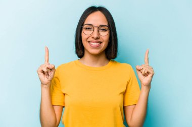 Mavi arka planda izole edilmiş genç İspanyol kadın iki parmağı da boş bir alan gösteriyor..