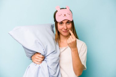Mavi arka planda izole edilmiş pijama giyen genç beyaz kadın sanki seni davet ediyormuş gibi seni işaret ediyor..