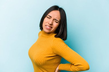 Genç İspanyol kadın mavi arka planda izole edilmiş sırt ağrısı çekiyor..