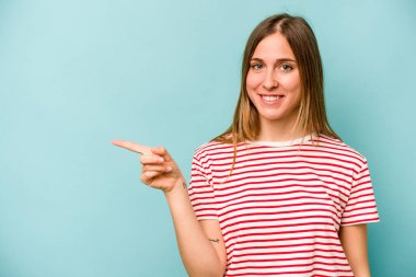 Mavi arka planda izole edilmiş genç beyaz kadın işaret parmağıyla işaret ederek gülümsüyor..