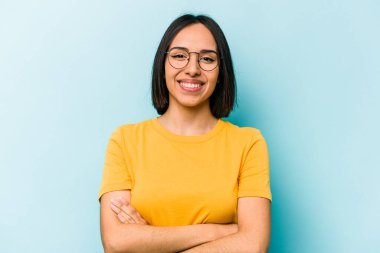 Mavi arka planda kendini güvende hisseden, kararlılıkla kollarını kavuşturan genç İspanyol kadın..