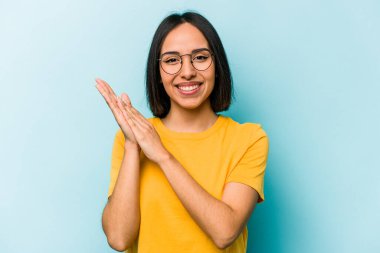 Mavi arka planda izole edilmiş genç İspanyol kadın enerjik ve rahat hissediyor, ellerini ovuşturuyor..