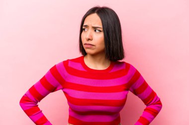 Pembe arka planda izole edilmiş genç İspanyol kadın kafası karışmış, şüpheli ve güvensiz hissediyor..