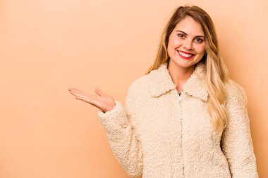 Beyaz tenli genç bir kadın, bej arka planda izole edilmiş bir şekilde bir avuç içinde fotokopi alanı ve belinde bir el daha gösteriyor..