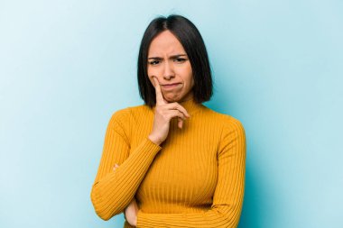 Latin kökenli genç bir kadın, mavi arka planda izole edilmiş. Bir strateji planlıyor, bir iş yolu düşünüyor..