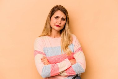 Beyazlı genç bir kadın bej arka planda izole edilmiş. Mutsuz, iğneleyici bir ifadeyle kameraya bakıyor..