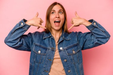 Pembe arka planda izole edilmiş genç beyaz kadın parmaklarıyla bir cep telefonu hareketi gösteriyor..