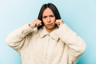 Mavi arka planda izole edilmiş genç İspanyol kadın bir tartışma yüzünden yumruk atıyor, sinirleniyor, kavga ediyor..