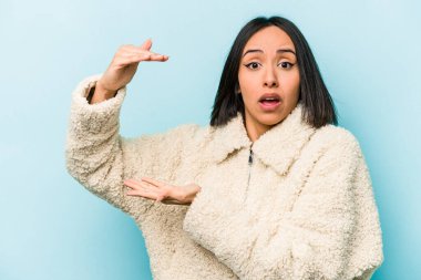 Mavi arka planda izole edilmiş genç İspanyol kadın elleri arasında bir kopya alanı tutarken şok ve hayrete düştü..