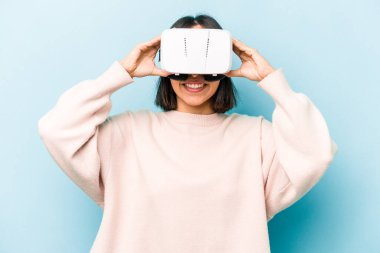 Mavi arka planda izole edilmiş sanal gözlük takan genç İspanyol kadın.