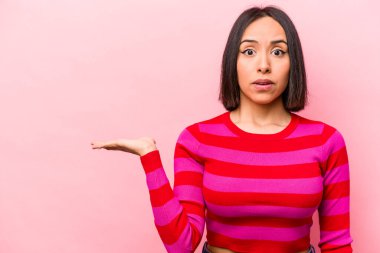 Pembe arka planda izole edilmiş genç İspanyol kadın avuç içi fotokopi alanını tutmaktan etkilenmiş..