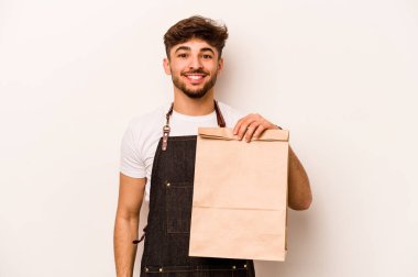 Beyaz arka planda izole edilmiş, mutlu, güler yüzlü ve neşeli bir paket taşıyan genç İspanyol tezgahtar..