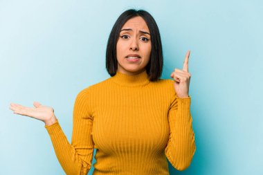 Genç İspanyol kadın mavi arka planda izole edilmiş ve elinde bir ürün tutuyor..