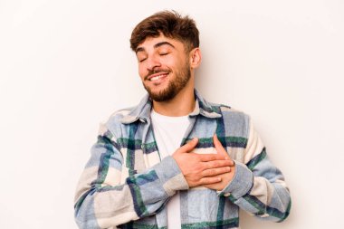 Beyaz arka planda izole edilmiş genç İspanyol bir adam, dost canlısı bir ifadeye sahip, avuçlarını göğsüne bastırıyor. Aşk konsepti.