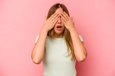 Pembe arka planda izole edilmiş genç beyaz kadın elleriyle gözlerini kapatmaktan korkuyor..