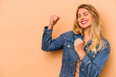 Beyazlı genç bir kadın bej arka planda izole edilmiş zafer sonrası yumruğunu kaldırıyor, kazanan konsept..