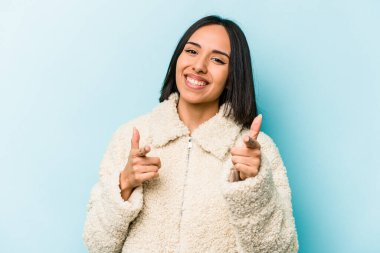 Mavi arka planda izole edilmiş genç İspanyol kadın parmaklarıyla ön tarafı işaret ediyor..