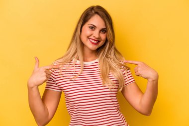 Sarı arka planda izole edilmiş genç beyaz kadın parmağını göstererek şaşırdı, geniş bir gülümsemeyle..