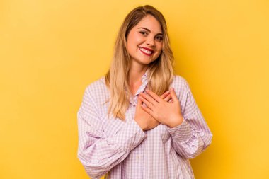Sarı arka planda izole edilmiş genç beyaz kadın, dost canlısı bir ifadeye sahip, avuçlarını göğsüne bastırıyor. Aşk konsepti.