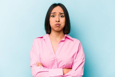 Mavi arka planda izole edilmiş genç İspanyol kadın yanakları patlatıyor, yorgun bir ifadesi var. Yüz ifadesi kavramı.