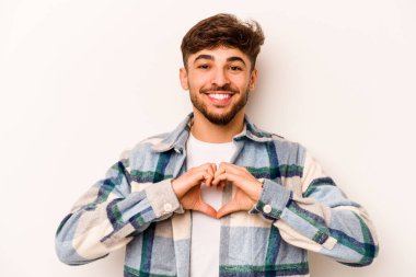 Beyaz arka planda izole edilmiş genç İspanyol adam gülümsüyor ve elleriyle kalp şeklini gösteriyor..