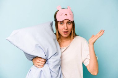 Mavi arka planda izole edilmiş pijama giyen beyaz bir kadın şaşırdı ve şok oldu..