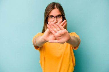 Mavi arka planda izole edilmiş genç beyaz bir kadın inkar jesti yapıyor.