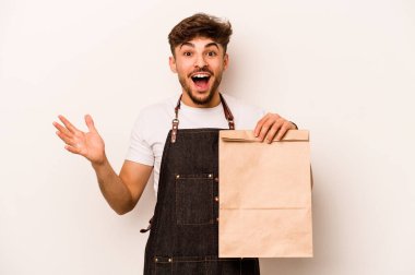 Beyaz arka planda izole edilmiş bir çanta taşıyan genç İspanyol tezgahtar hoş bir sürprizle karşılaşıyor, heyecanlı ve el kaldırıyor..