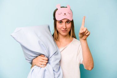Mavi arka planda izole edilmiş pijama giyen beyaz bir kadın bir numarayı parmağıyla gösteriyor..