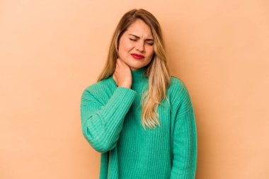 Beyazlı genç bir kadın bej arka planda izole edilmiş. Stres yüzünden boynu ağrıyor, masaj yapıyor ve elle dokunuyor..